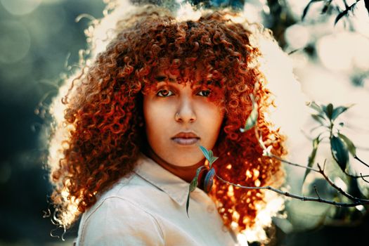 A captivating portrait of a young woman with curly hair amidst nature.