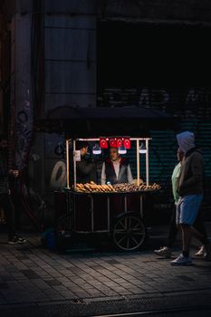 A vibrant night street scene in Istanbul featuring a vendor cart with local snacks and Turkish flags.