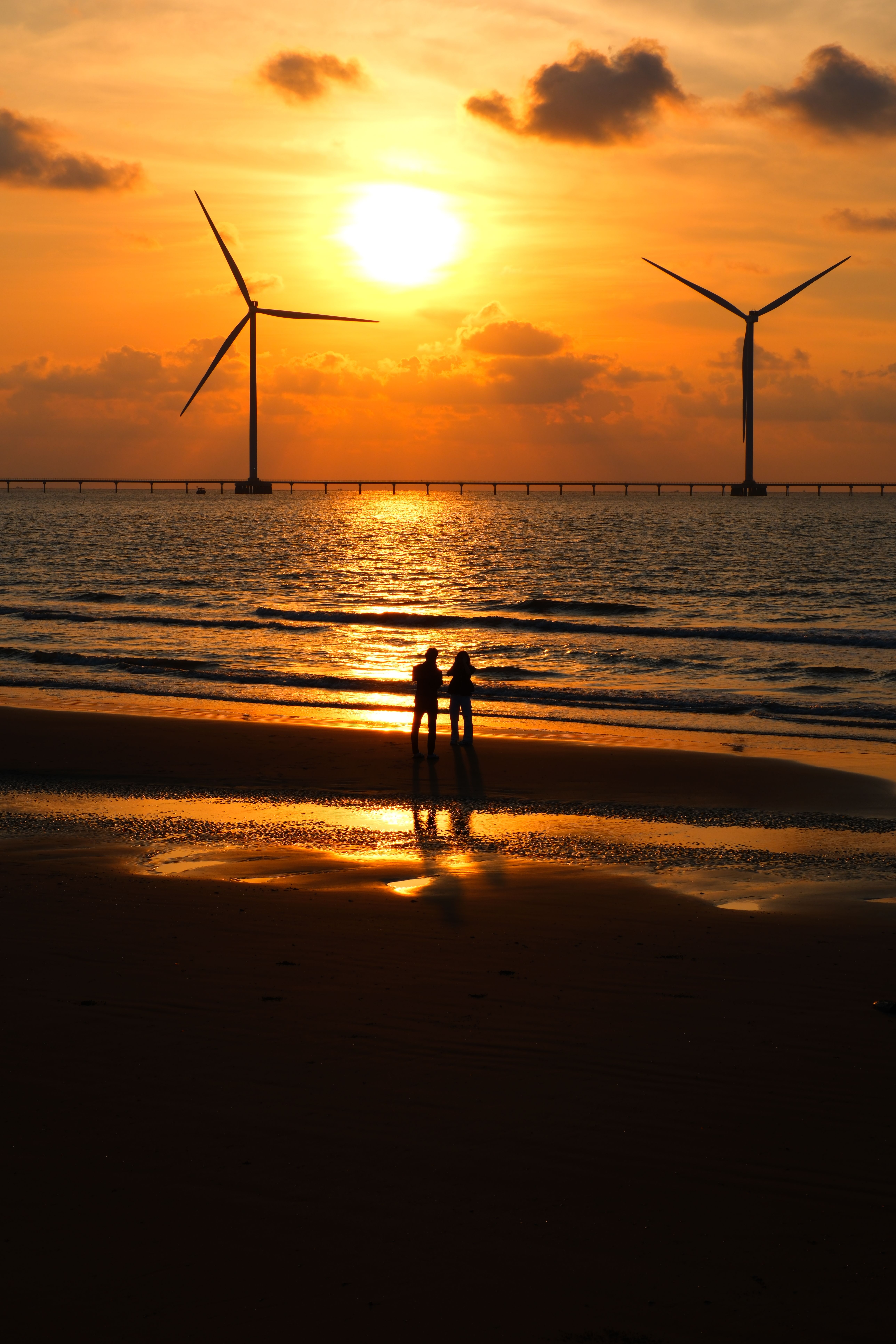 Couple on Beach with Wind Turbines at Sunset · Free Stock Photo