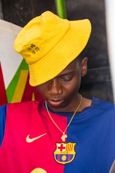 A stylish young man wearing a vibrant FC Barcelona jersey and yellow hat. Perfect for fashion and sports themed content.