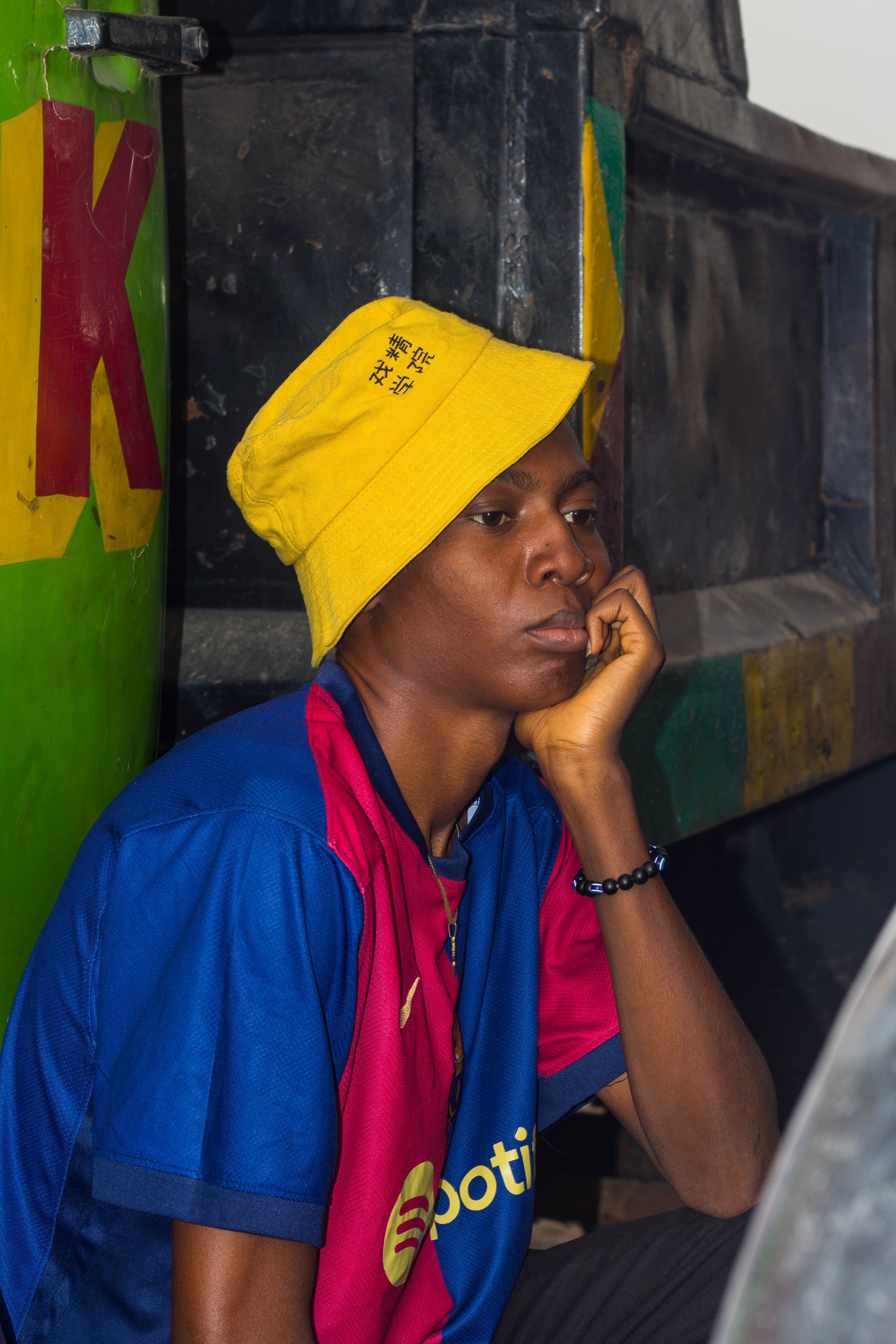 Person in yellow hat and blue shirt sits thoughtfully by colorful truck.