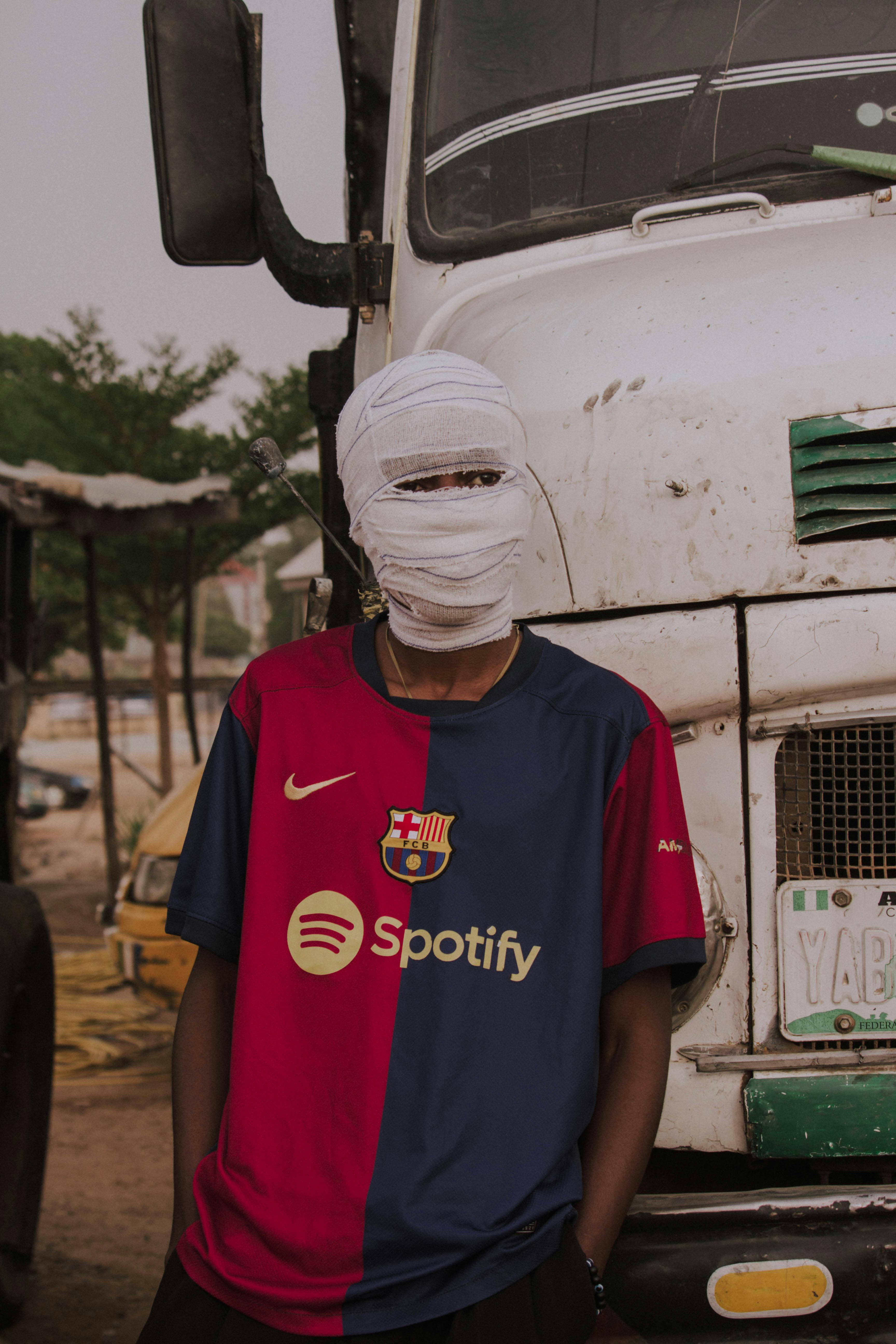 Masked Individual Posing by Large Truck in Urban Setting · Free Stock Photo