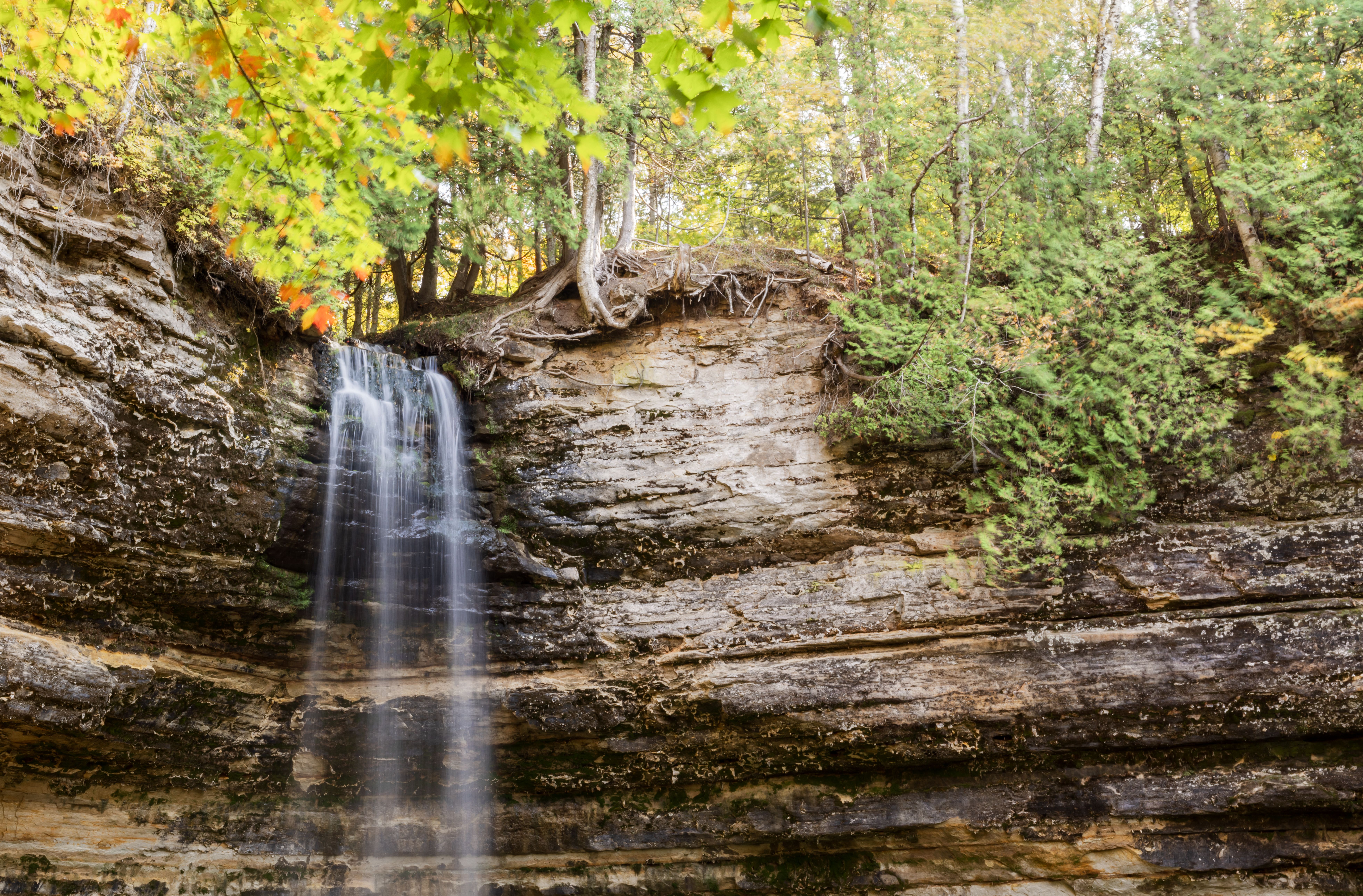 A tranquil waterfall cascading down rock layers surrounded by lush forest