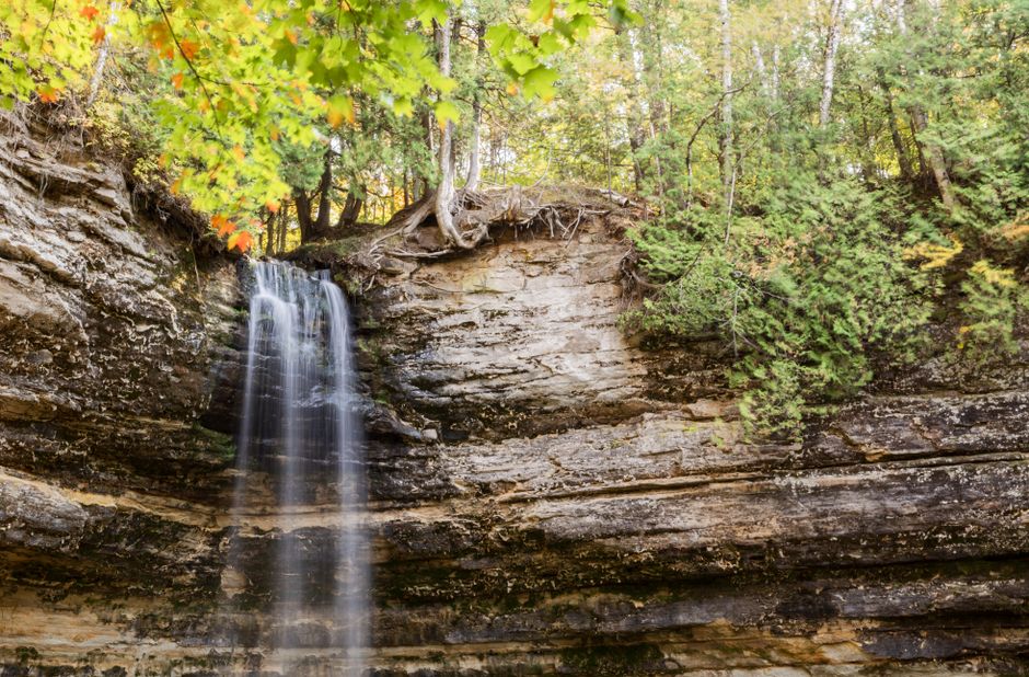 A tranquil waterfall cascading down rock layers surrounded by lush forest