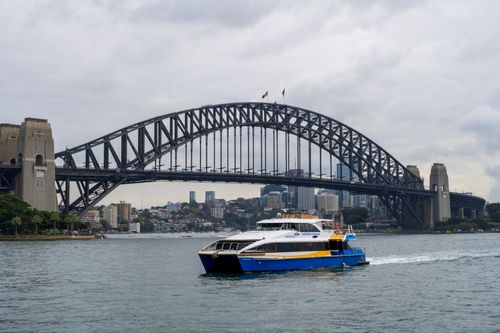 Free Scenic view of Sydney Harbour Bridge with a ferry boat cruising under cloudy skies. Stock Photo