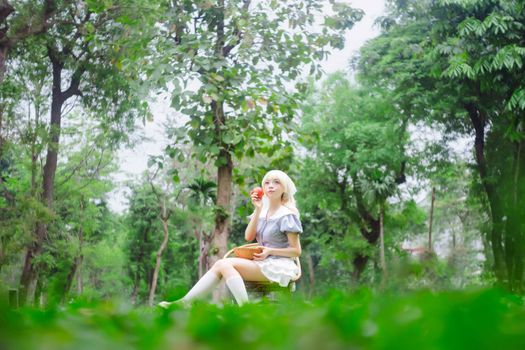 A young woman in cosplay enjoys a serene moment with an apple in a vibrant green park.