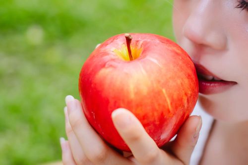 Free Close-up of a woman holding a bright red apple outdoors, highlighting healthy living and freshness. Stock Photo
