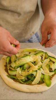 Hands arranging zucchini and Parmesan on a fresh pizza base.