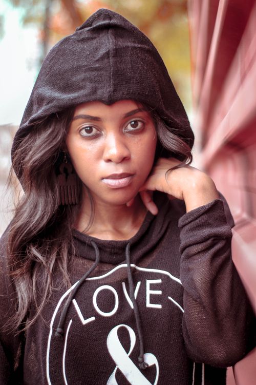 Free Stylish woman in a black hoodie gazes into the camera, outdoors with a serene expression. Stock Photo