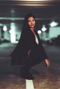 Young woman kneeling confidently in an urban parking garage. Stylish and modern vibe.