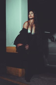 Woman in dark attire posing dramatically in low light urban environment.