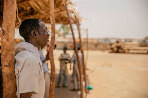 Free A man stands under a rustic wooden structure in Kano, Nigeria, observing the scene outdoors. Stock Photo