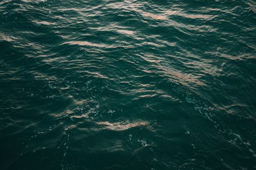 Free Calm ocean surface reflecting warm sunset hues in Ilhabela, Brazil. Perfect for nature lovers. Stock Photo