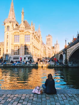 Scenic view of Gent canals with historic architecture and a relaxing visitor.