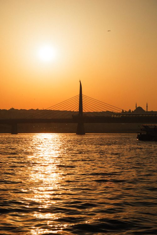 Free Stunning sunset over water with a silhouette of a bridge and cityscape in the background. Stock Photo