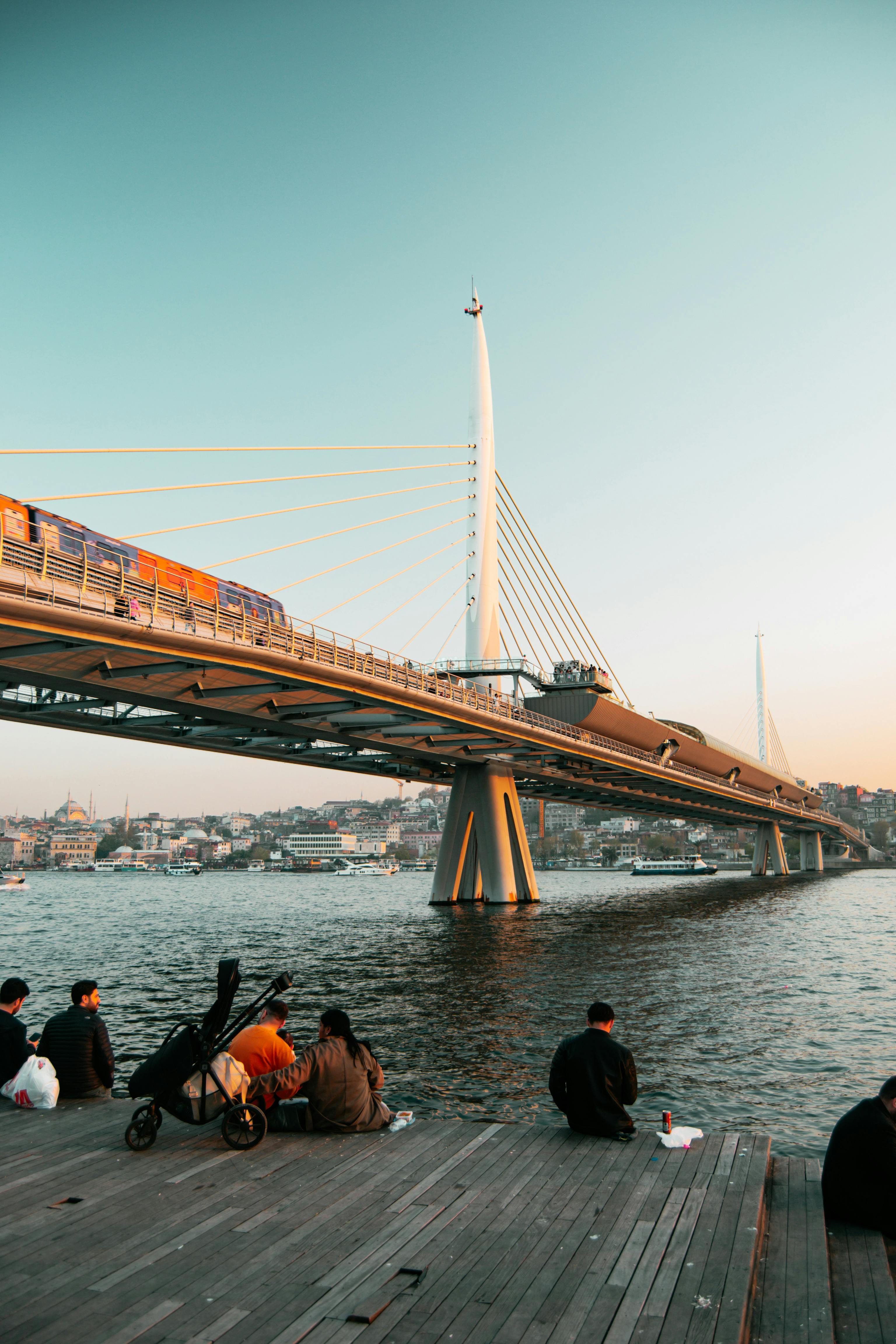 Gratuit Vue panoramique du pont du métro de la Corne d'Or avec des gens se relaxant au bord de l'eau pendant le coucher du soleil à Istanbul, en Turquie. Photos