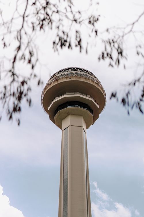 Free Upward view of Atakule Tower, Ankara, Türkiye, framed by tree branches against the sky. Stock Photo