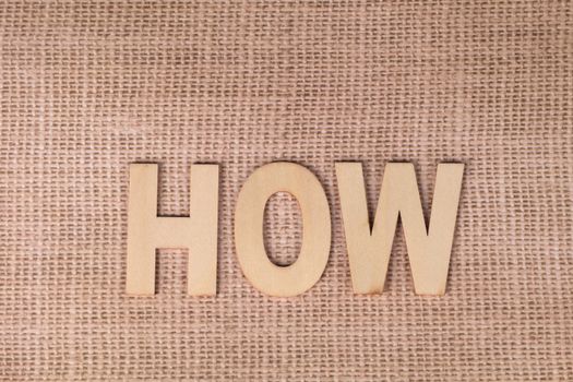 Word 'HOW' formed with wooden letters on textured burlap surface.