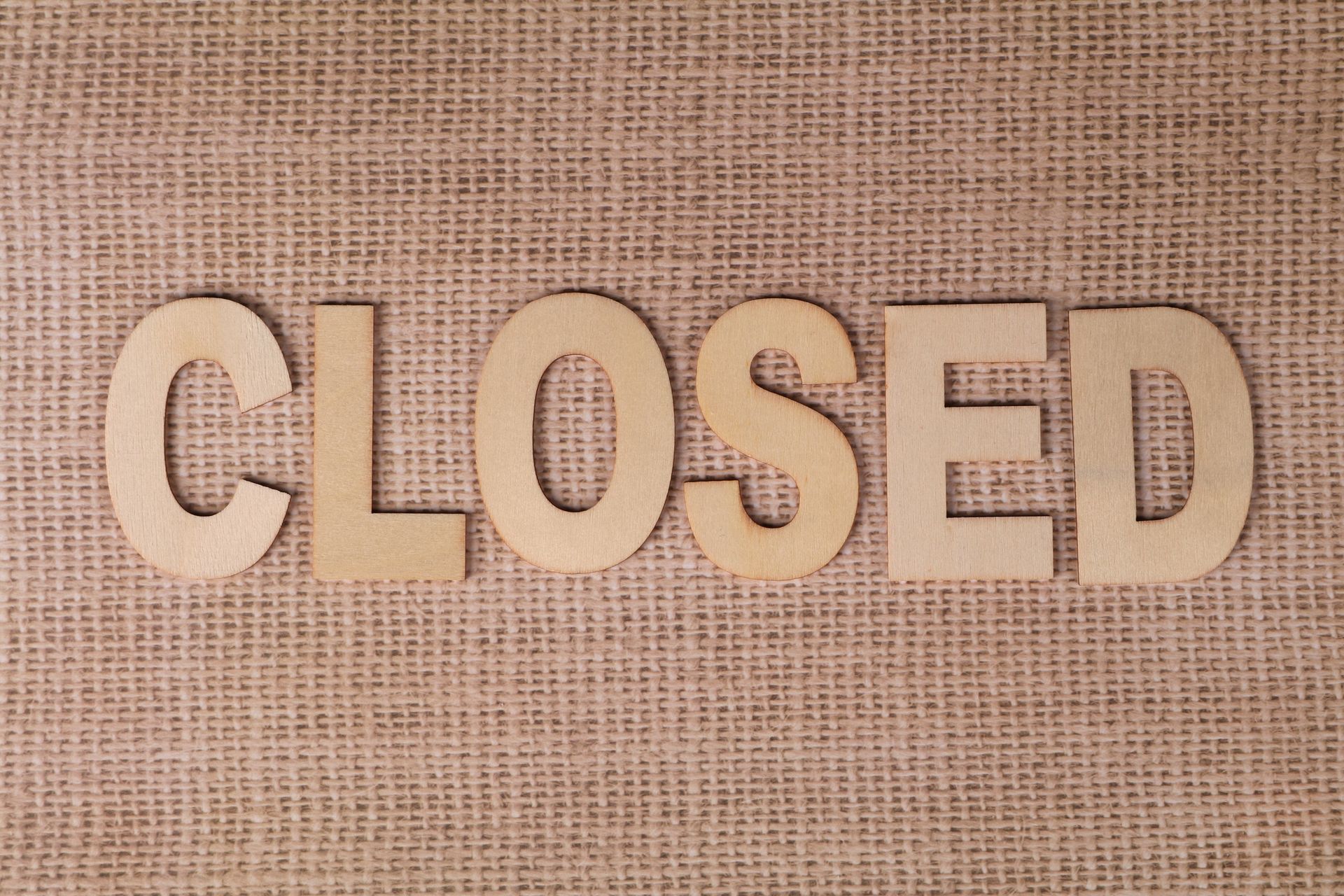 Wooden "Closed" sign on burlap fabric, ideal for business closure themes.