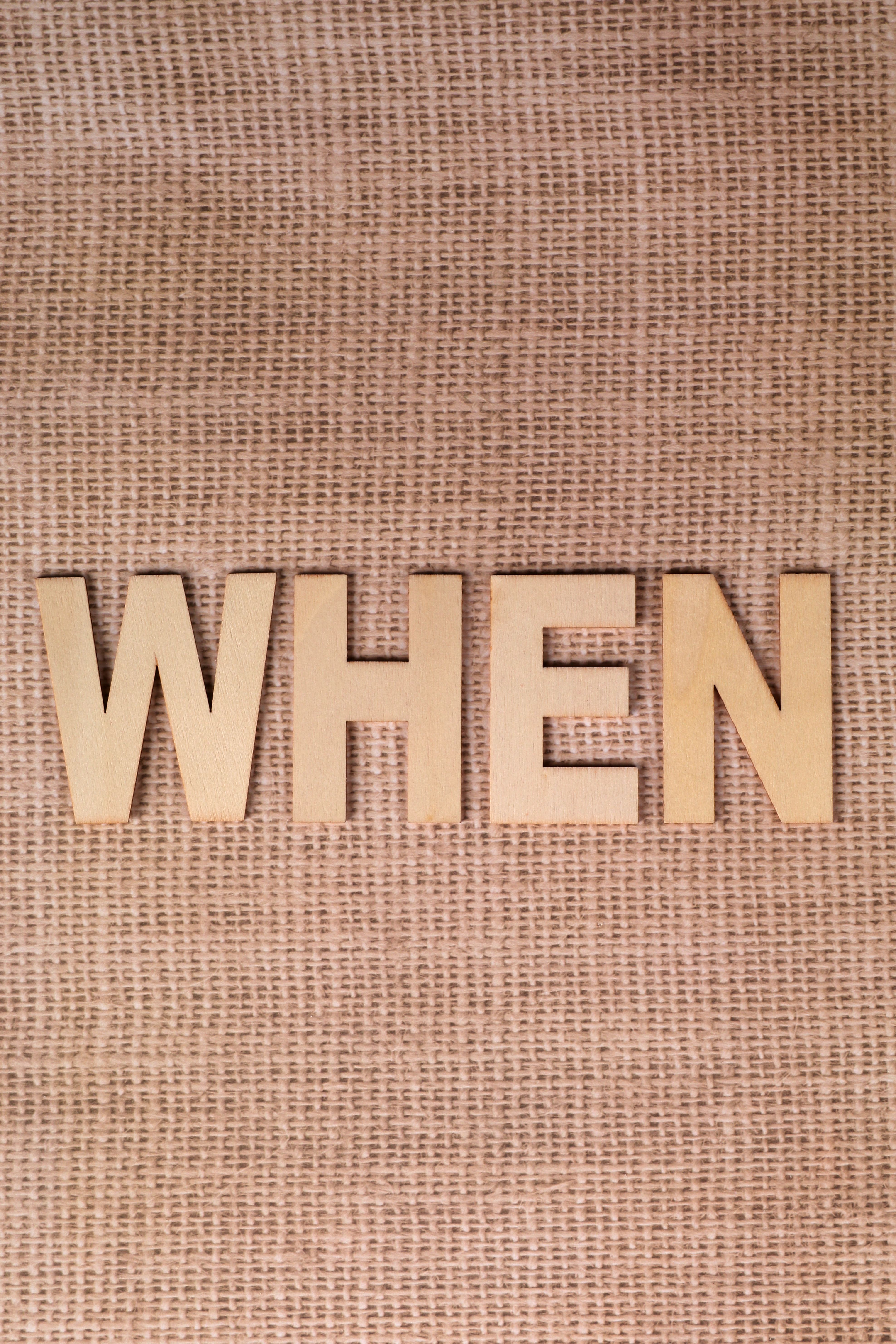 Wooden letters spelling 'WHEN' on a textured burlap fabric surface.