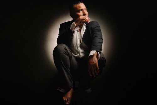Free A contemplative man in a suit sits in dramatic lighting against a dark background. Stock Photo