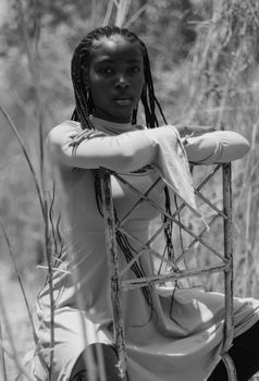 Black and white portrait of a woman seated on a chair amidst tall grass.