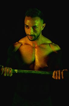 Intense close-up of a muscular man lifting a barbell in a dark, moody setting.