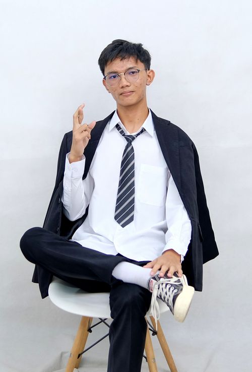 Free Young man sitting confidently in business attire, making a peace sign gesture against a minimalist background. Stock Photo