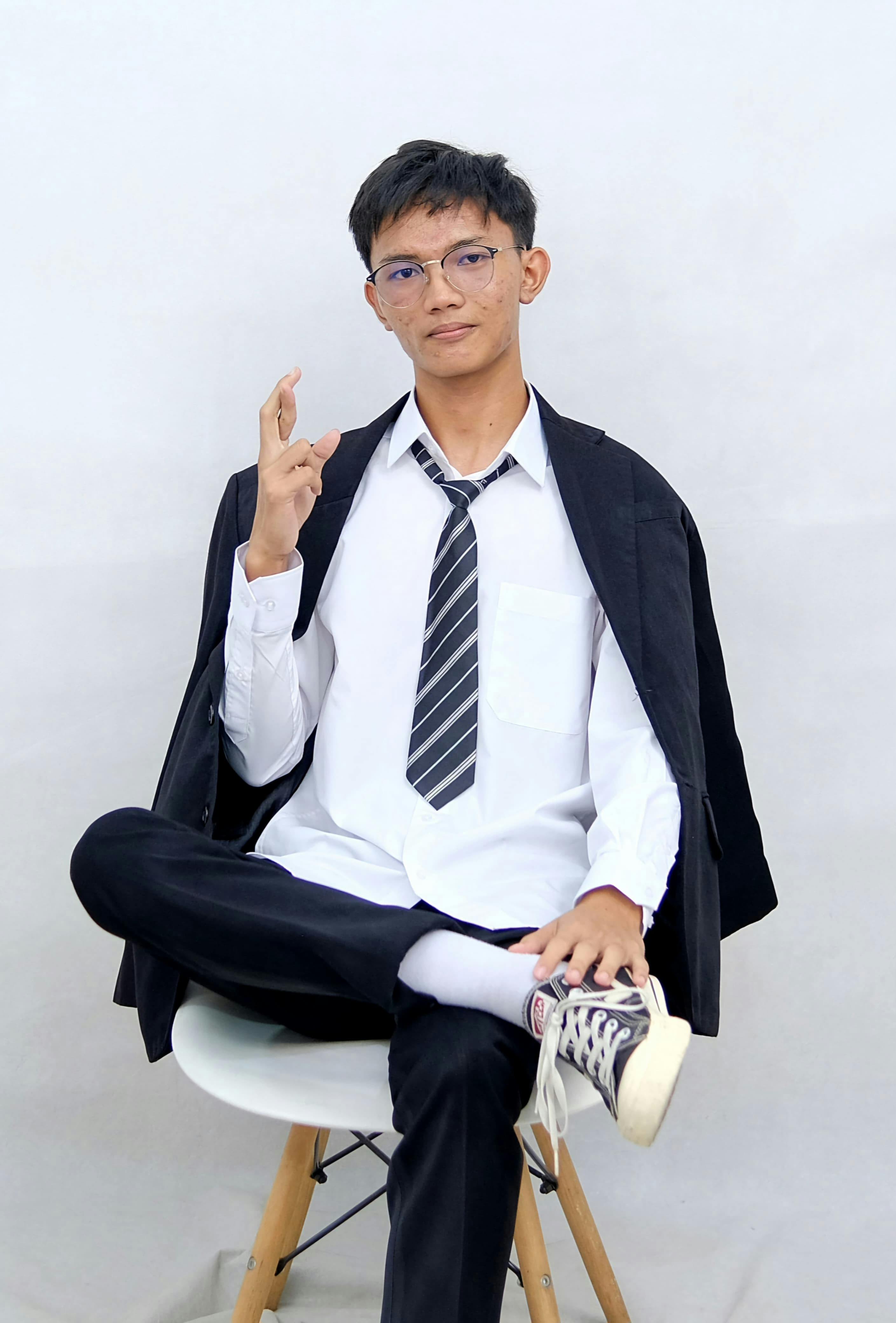 Gratis Pria muda duduk dengan percaya diri dalam pakaian bisnis, membuat gerakan tanda perdamaian dengan latar belakang minimalis. Foto Stok