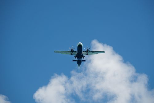 Free An airplane flying against a clear blue sky with fluffy white clouds. Captured from below. Stock Photo