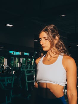 A woman in a gym setting, highlighted by dramatic lighting, showcasing determination and fitness focus.