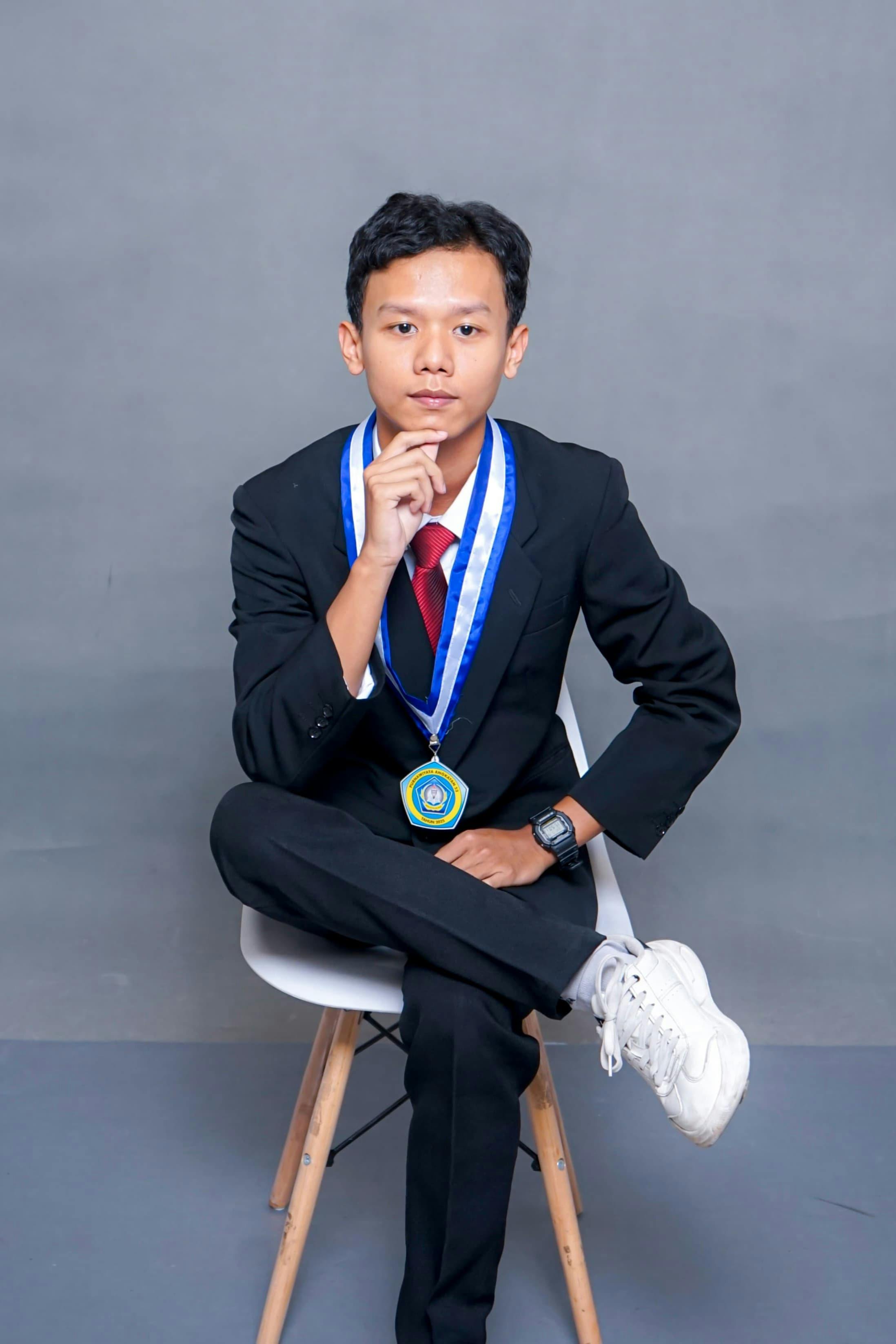 Confident young man in formal attire with a medal posing seated on a chair.