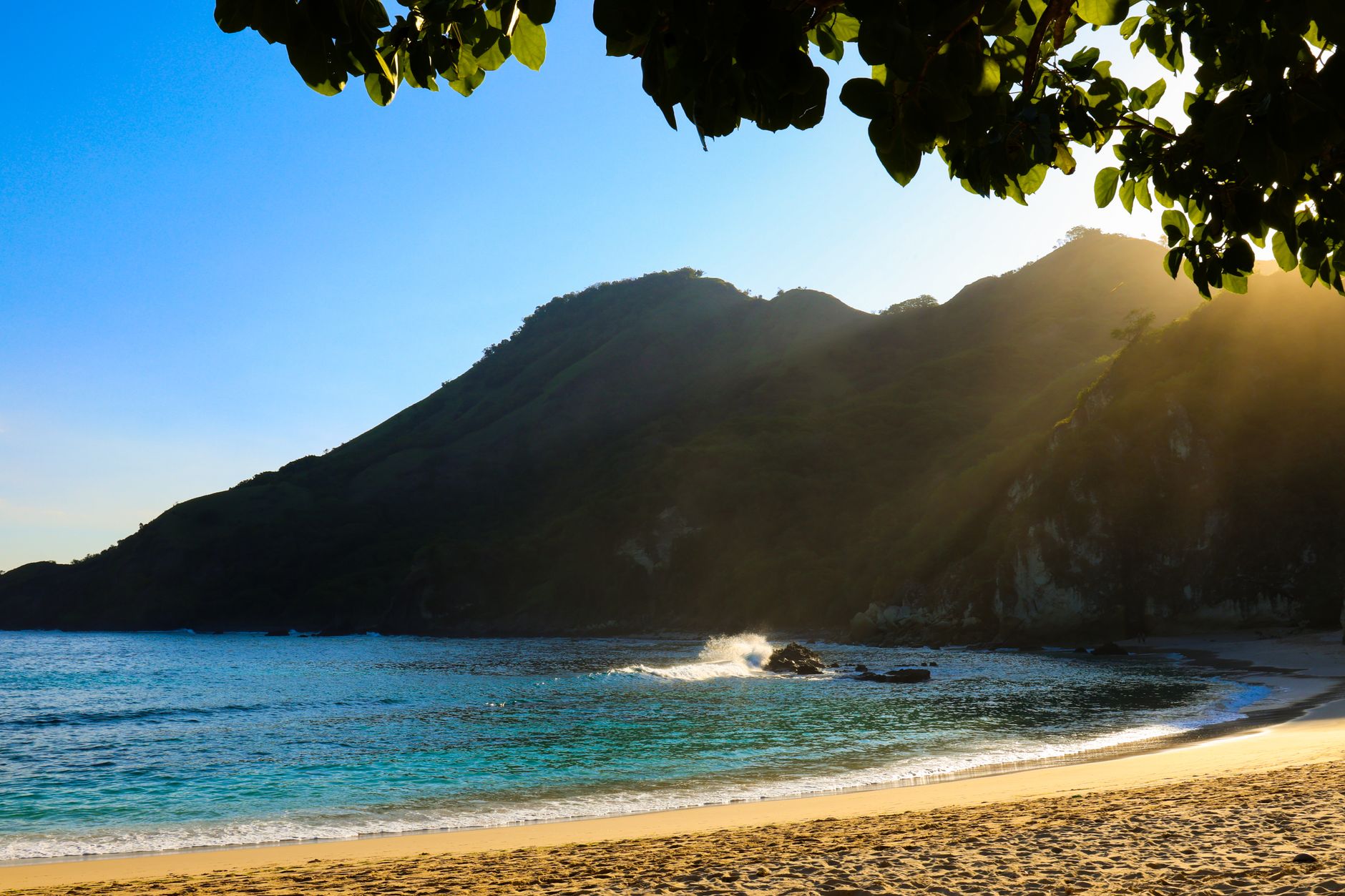 Tranquil beach scene in East Nusa Tenggara, Indonesia, featuring sunlit hills and calm waters.