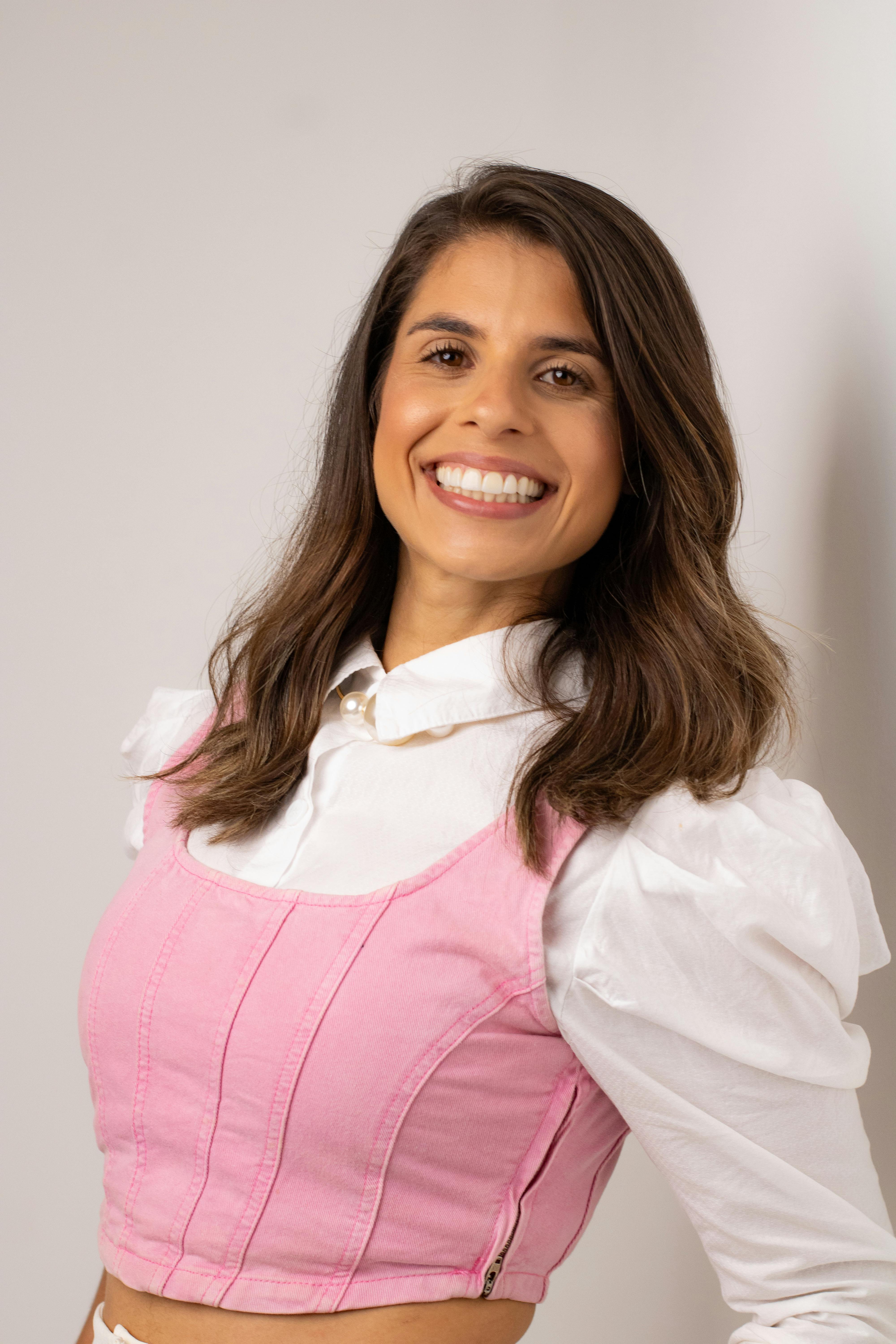 Portrait of a smiling woman in a pink and white outfit, exuding confidence and joy.