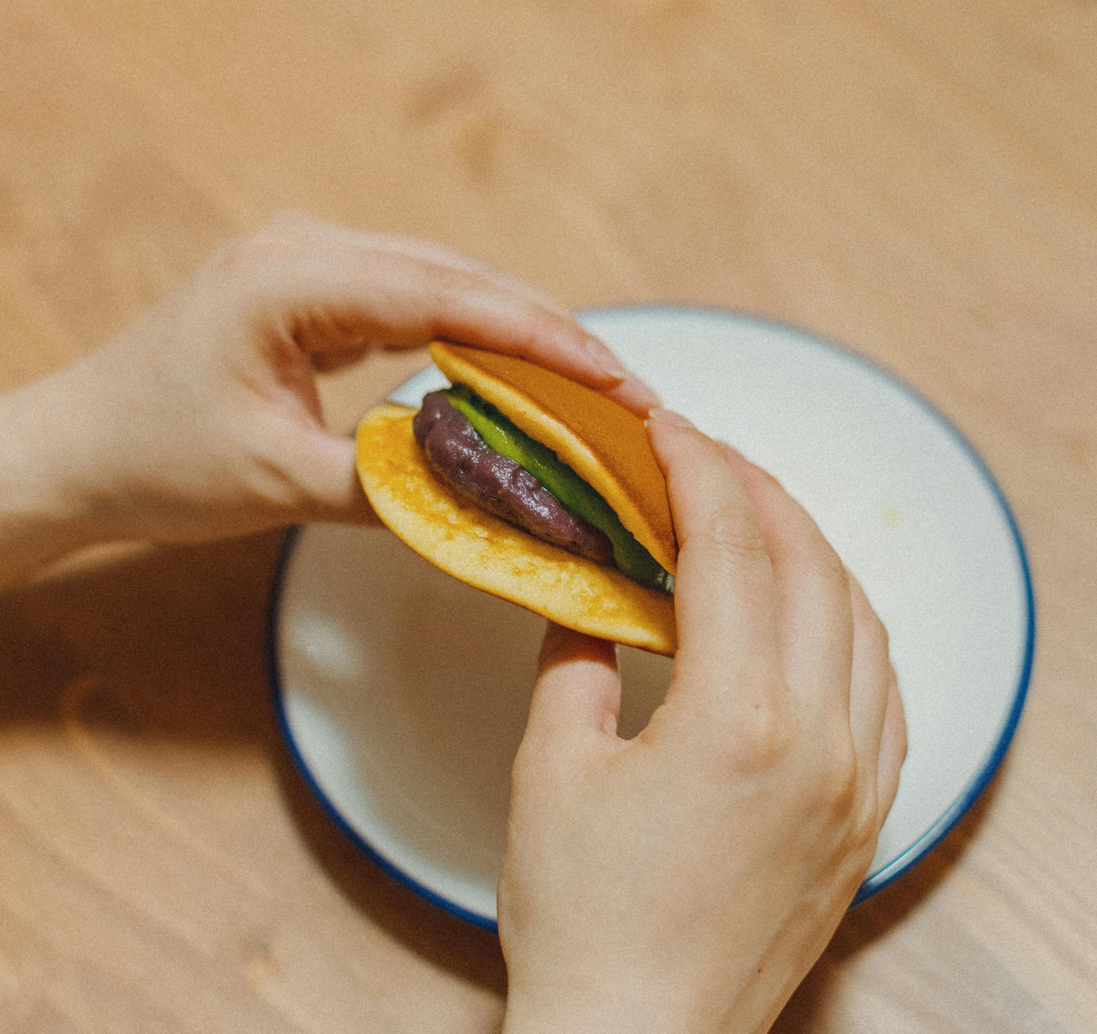 Hands holding a Japanese dorayaki filled with matcha and red beans on a plate.