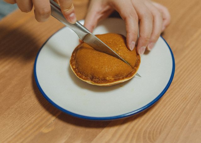 Close-up of hands cutting a dorayaki pancake revealing sweet filling, on a white plate. Authentic Japanese dessert.