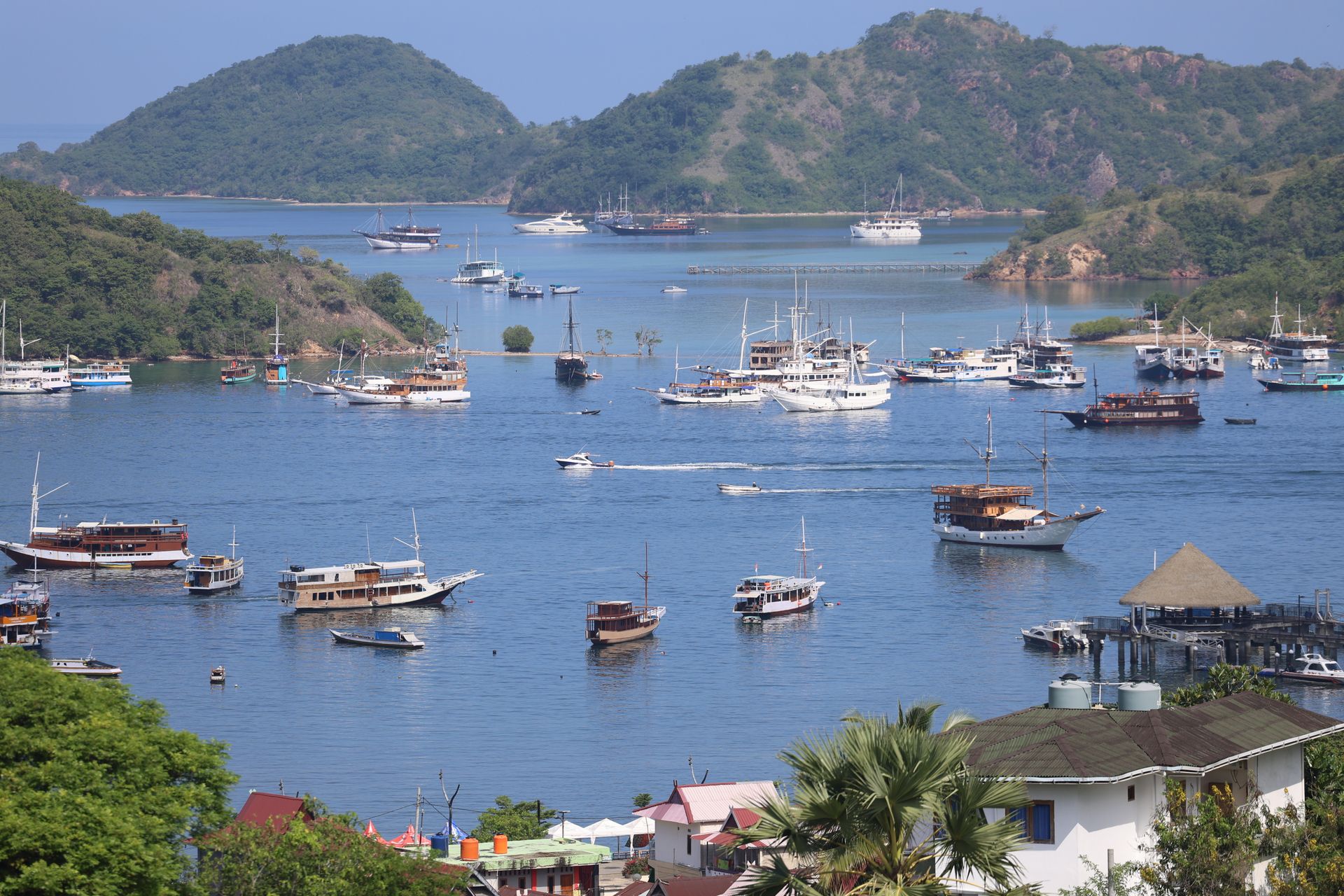 Explore the picturesque harbor of Labuan Bajo, Indonesia, bustling with boats against lush hills.