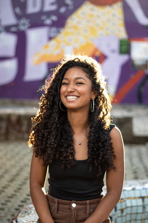 Free Portrait of a young woman with curly hair smiling in an urban environment with colorful graffiti. Stock Photo