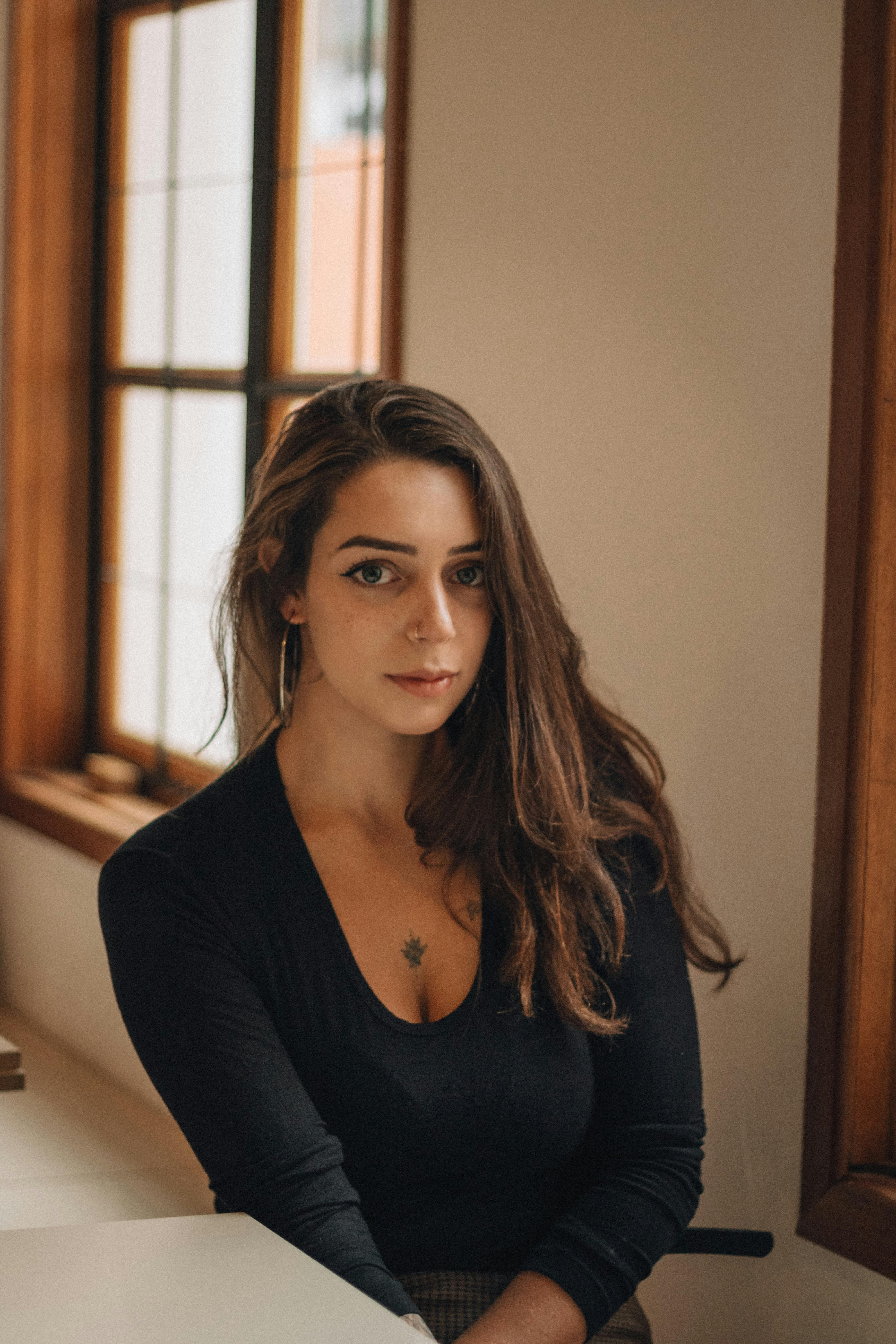 무료 실내 창가에 앉아 있는 긴 머리를 한 젊은 여성의 우아한 초상화입니다. 스톡 사진