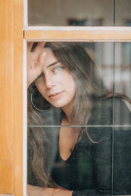 Free Portrait of a woman gazing thoughtfully through a window indoors. Stock Photo