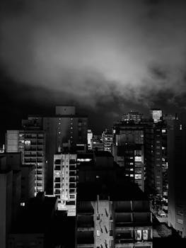 Moody city skyline at night in black and white, showcasing urban architecture.