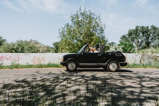 A black convertible car with a couple driving through a scenic route on a sunny day.