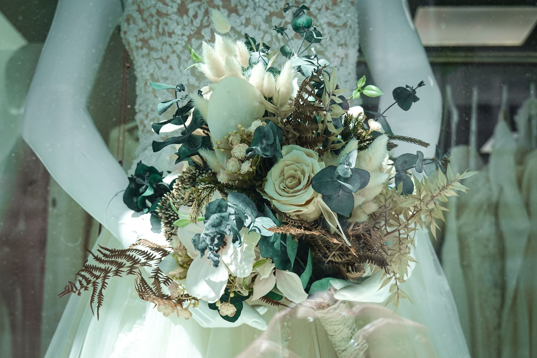 Close-up of a luxurious white floral bridal bouquet held by a mannequin in a wedding dress display.