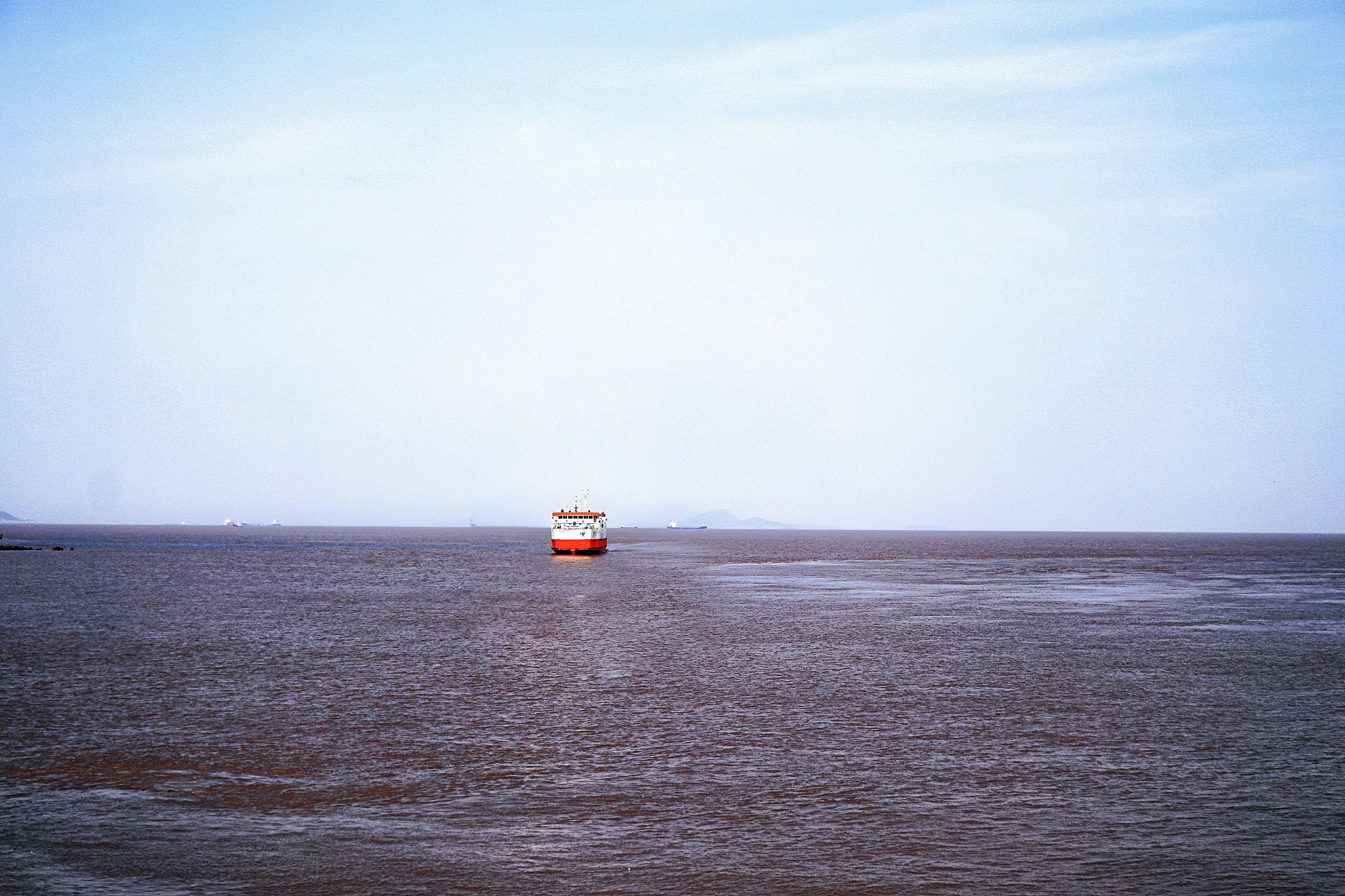 Distant cargo ship sailing on a vast, calm sea under a clear, blue sky.