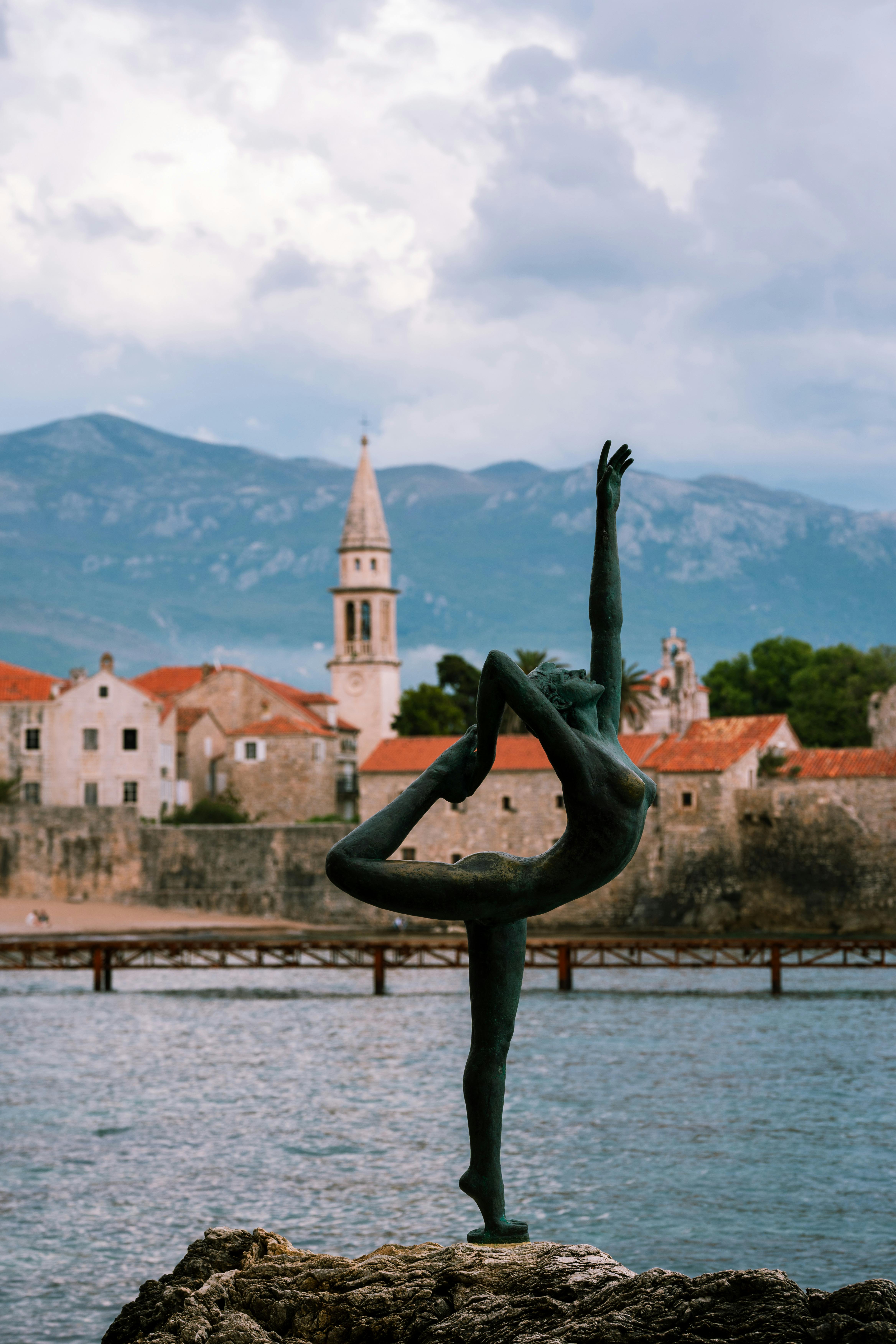 Ballet statue by the Adriatic Sea with historic Budva town and mountains in the background.