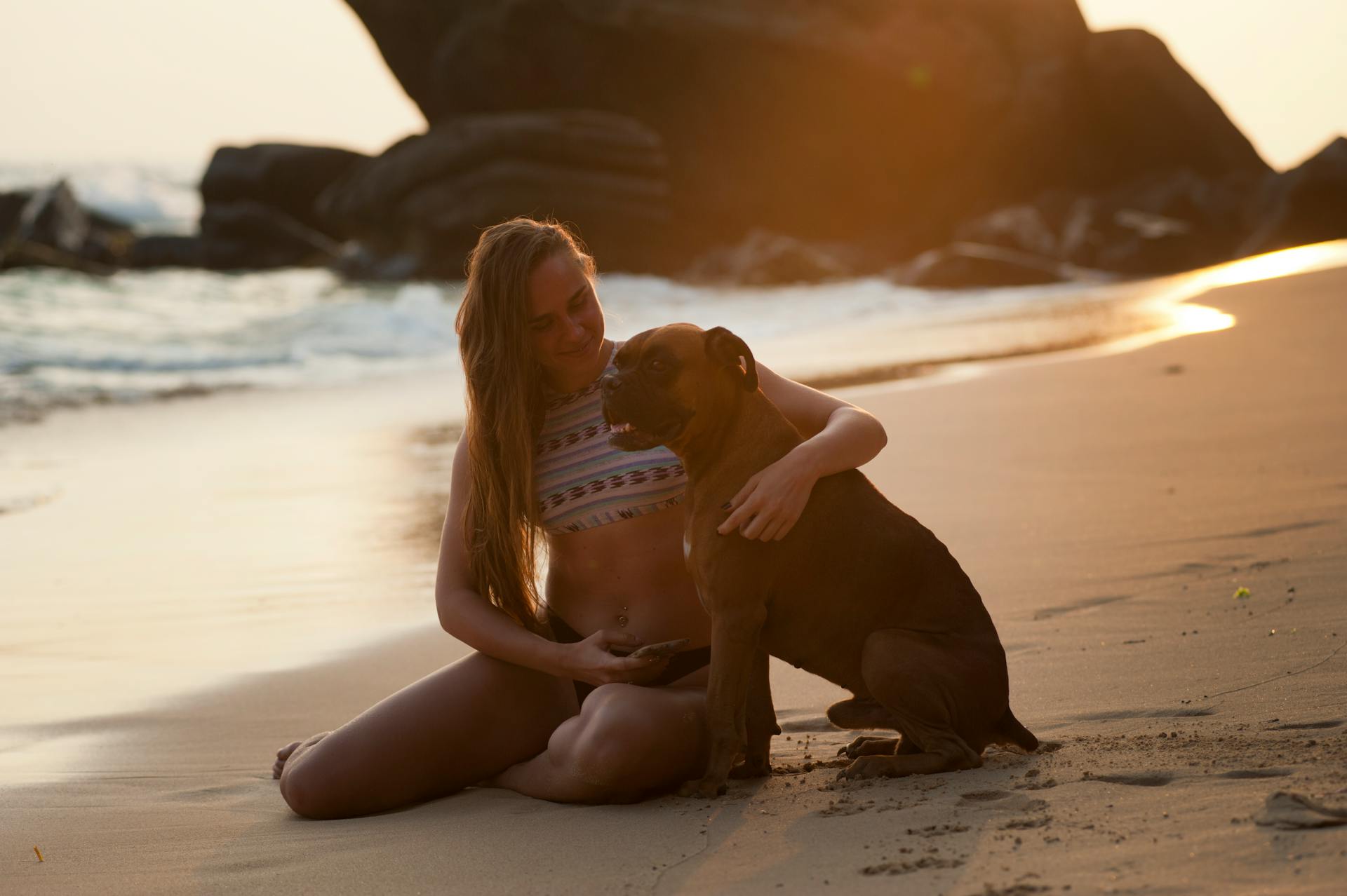 Une femme tenant un chien boxeur sur la plage