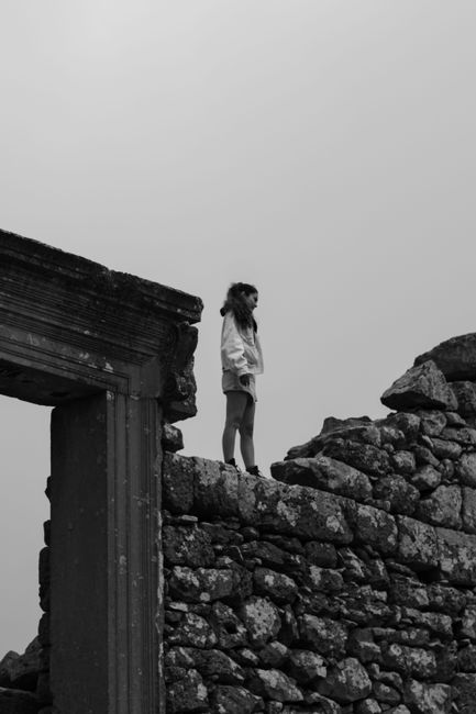 A woman stands on ancient ruins, exuding a sense of solitude and reflection.