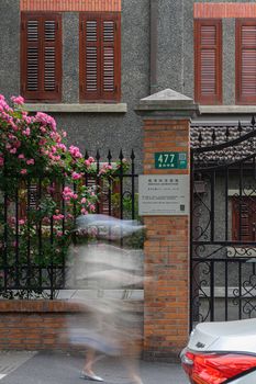 Blurred motion of a person near an old building with pink flowers.