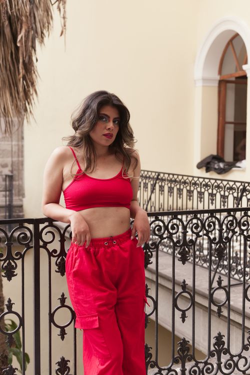 Free Stylish adult woman in red crop top and pants posing on ornate balcony with historical architecture. Stock Photo