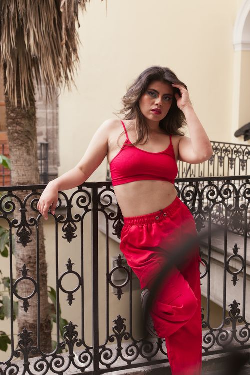 Free Fashionable young woman in red crop top and pants posing on a decorative balcony outdoors. Stock Photo